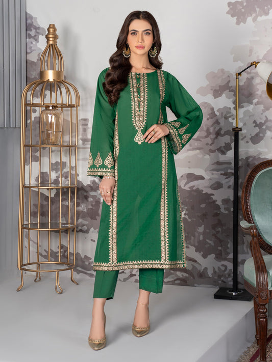 Woman wearing a green printed lawn suit with intricate embroidery, standing in a stylish room with elegant decor.